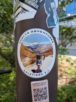 Street sticker A round sticker showing a moka pot on a camp stove set against a snowy mountain backdrop. It features a white border with the text '#DELYS ADVENTURES' and 'GALATIANS 4:7'.