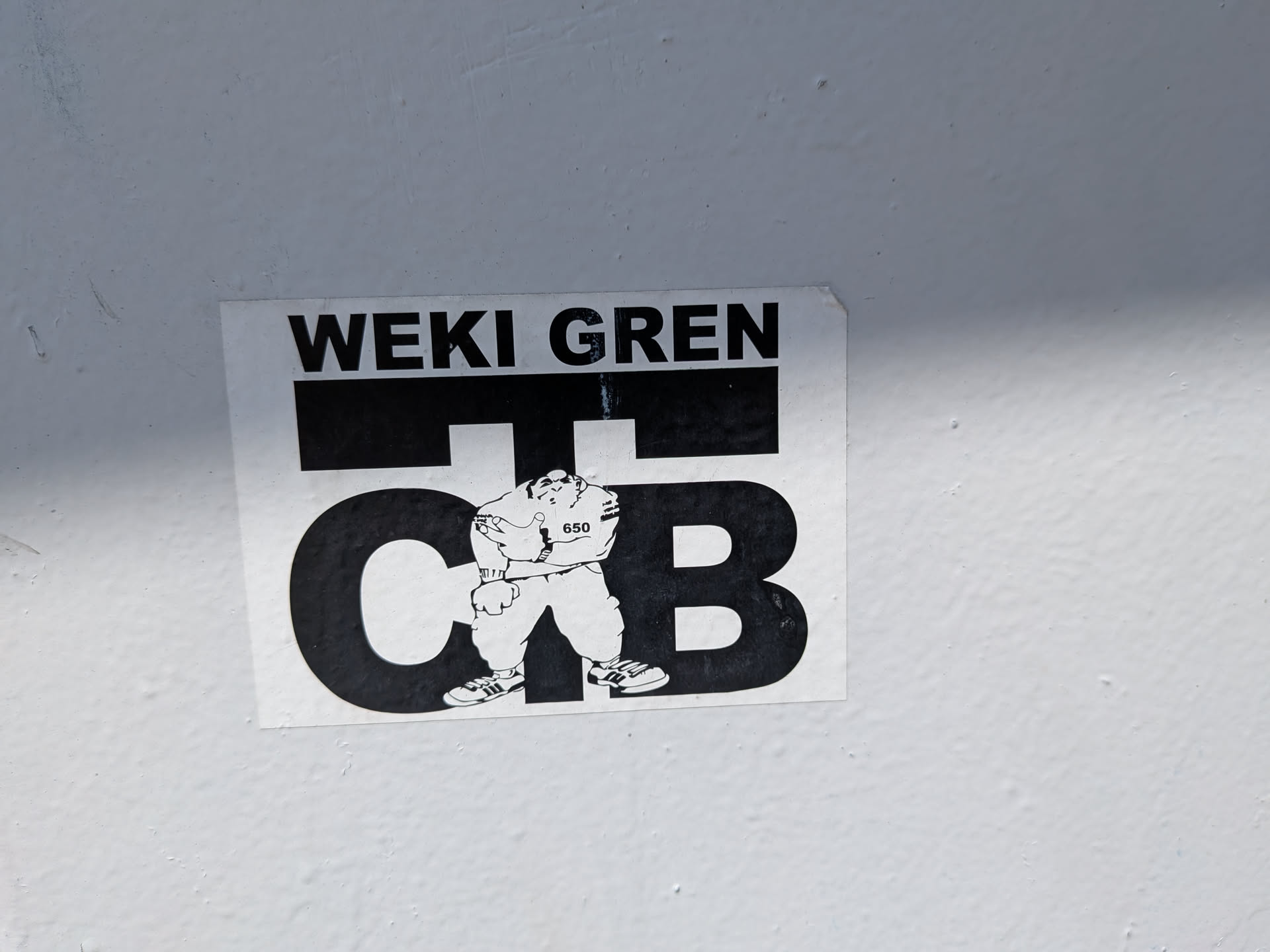 A rectangular black and white sticker. It displays the text 'WEKI GREN' above large stylized letters 'C T B'. In the center stands a cartoon b-boy character wearing sneakers and a shirt labeled '650'.