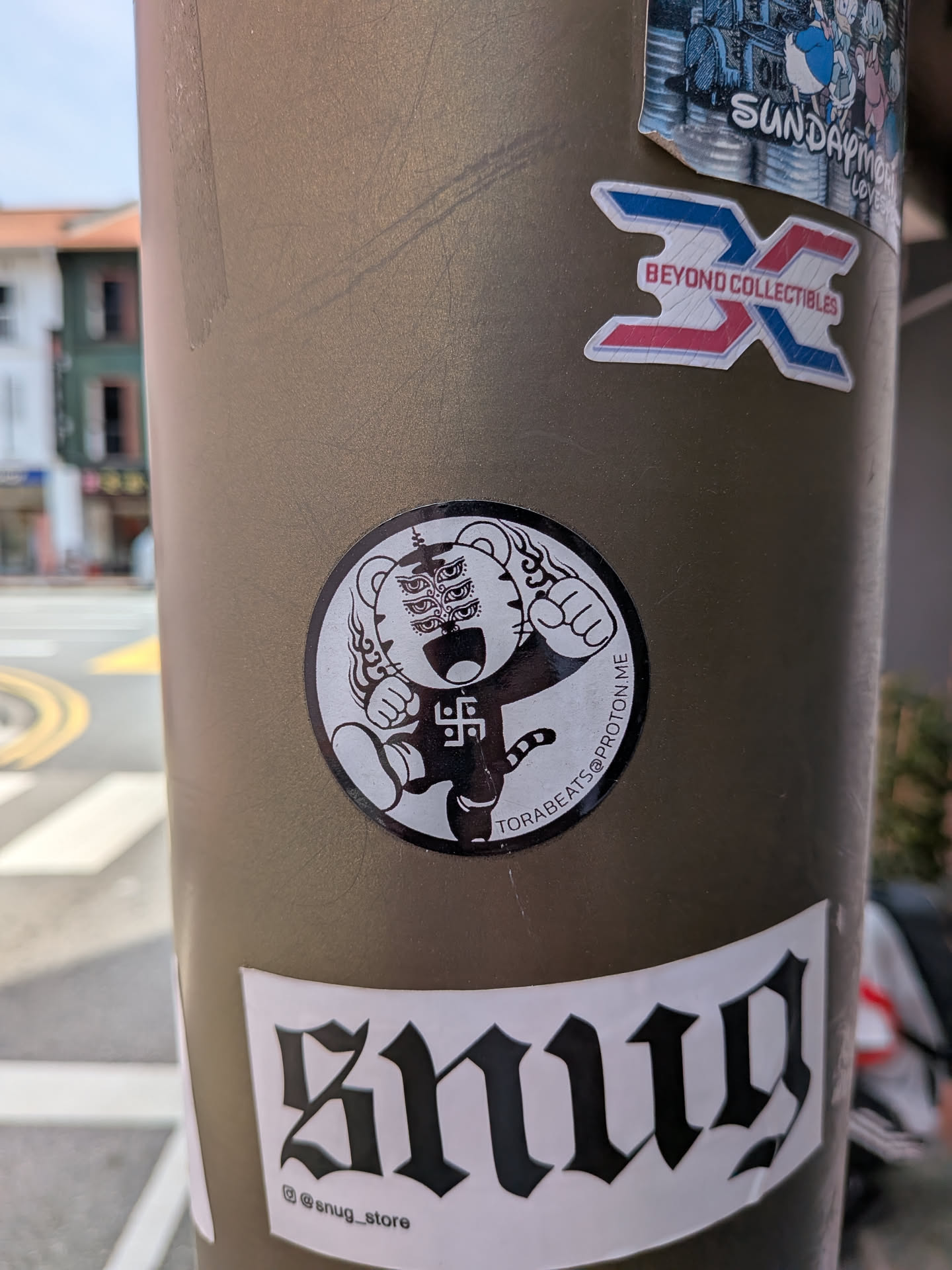 A circular black-and-white sticker showing a stylized tiger character with six eyes, raised fists, and a manji symbol on its chest. Includes the text 'TORABEATS@PROTON.ME' along the edge.