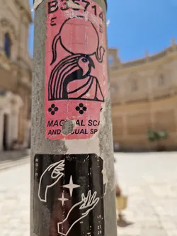 A pink sticker featuring a stylized figure carrying a large orb on its head. The style is reminiscent of ancient Egyptian art with bold lines and simplified shapes. Below the main figure, there are four small, evenly spaced dots arranged in a square pattern. Partial text on the sticker reads  "MAGICAL SCA... AND VISUAL SP... ". Another smaller black and white sticker is below featuring two hands cradling a star. 