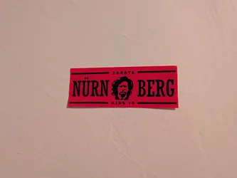 Street sticker Rectangular red sticker featuring black text and graphics. The word 'NÜRNBERG' is divided by a central stencil portrait of a bearded man with curly hair. 'ZARATE' is printed at the top and 'KIDS '14' at the bottom, bordered by black lines.