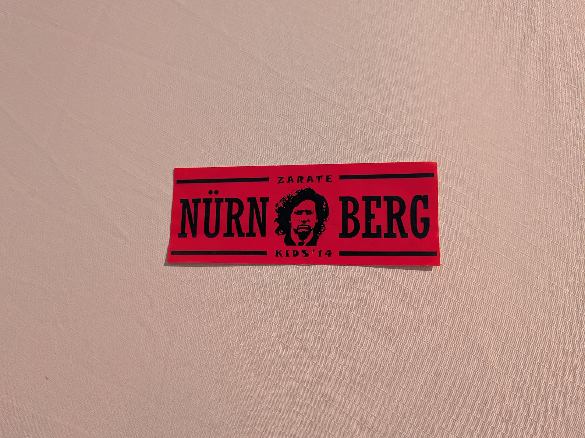 Rectangular red sticker featuring black text and graphics. The word 'NÜRNBERG' is divided by a central stencil portrait of a bearded man with curly hair. 'ZARATE' is printed at the top and 'KIDS '14' at the bottom, bordered by black lines.