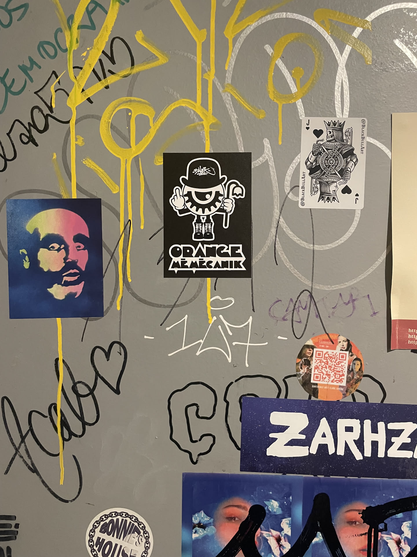 A rectangular black sticker featuring a stylized character in white. The character wears a bowler hat with the word 'SULK!' written on it, a suit, and holds a cane. Its left eye is replaced by a gear, and it wears a monocle over its right eye. The character is making a 'middle finger' gesture with its right hand. Below the character, in a blocky, somewhat distressed font, are the words 'ORANGE MEMECHANIK'. The overall aesthetic is stark black and white, reminiscent of graphic novel art or street art.