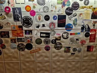 The image shows a variety of round and rectangular stickers affixed to a wall.  Many of the stickers feature logos or designs, while some have text. The stickers showcase a range of styles and themes. One circular sticker prominently features the text "VALOARE PLUS".