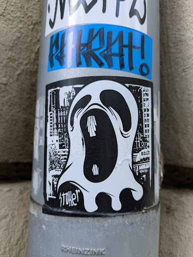 Street sticker The sticker showcases a white ghost-like figure with a gaping mouth, set against a background of a cityscape. The sticker has a monochrome scheme, with the figure primarily in white and the background in black. Text is visible at the bottom of the image that seems to read 'stoker'.