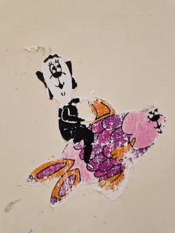 Street sticker This sticker shows a simple line drawing of a dog sitting on a larger, colorful fish.  The style is childlike and playful. The sticker appears to be slightly worn or weathered.