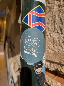 Street sticker This is a round sticker with two interlocked smiley faces on the top and the text "kollektiv spieltag" below the faces, likely advertising a gaming event or group.