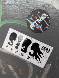 Street sticker The sticker contains a series of stylized black shapes reminiscent of figures or objects, set against a backdrop of white dots. It has a playful and somewhat abstract design.