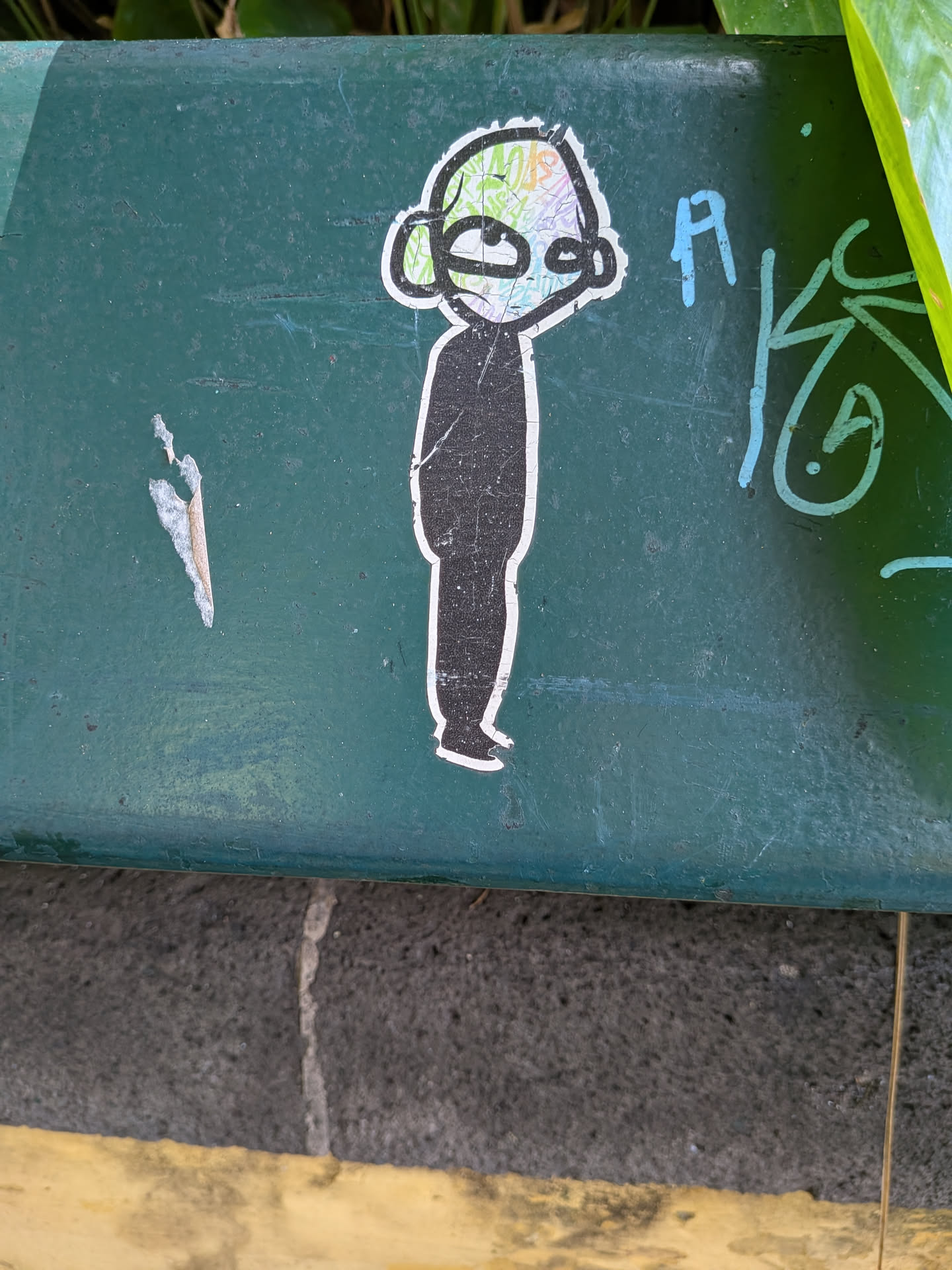 Die-cut sticker of a minimalist figure. Features a solid black body and a head filled with colorful, abstract graffiti scribbles. Outlined in white on a green background.