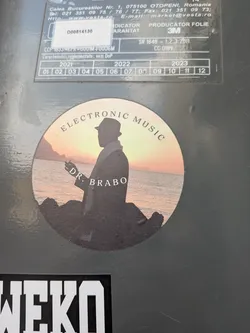 Street sticker A circular sticker depicting a dark silhouette of a man in a fedora and coat standing on rocks, looking out at a sunset over the ocean. The text 'ELECTRONIC MUSIC' is arched at the top, and 'DR. BRABO' is written across the center.