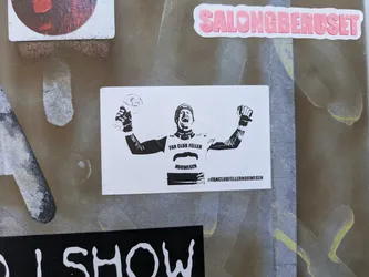 Street sticker The sticker features a black and white graphic of a male athlete, possibly a skier, with a helmet and sporting gear, raising his arms in triumph. He holds a trophy in his left hand and a clenched fist in his right. Below his image, the text 'FAN CLUB FELLER' is visible, followed by a stylized mustache graphic, and then 'NORWEGEN'. At the very bottom, a hashtag '#FANCLUBFELLERNORWEGEN' is displayed.
