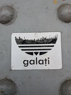 A rectangular white sticker depicting a black Adidas trefoil logo parody, where the top leaf is replaced by the Galați city skyline silhouette. The lowercase text 'galați' is printed below.