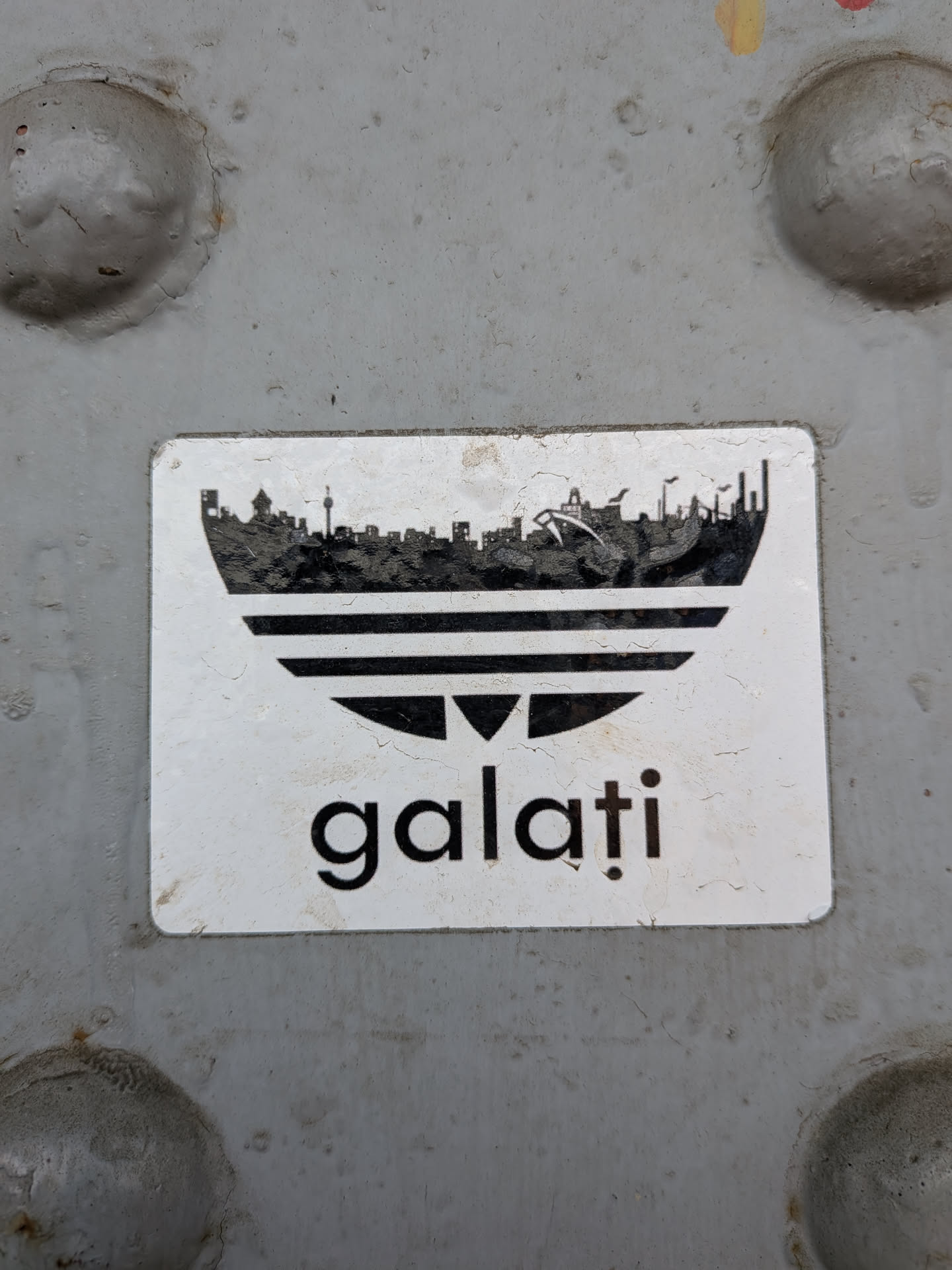 A rectangular white sticker depicting a black Adidas trefoil logo parody, where the top leaf is replaced by the Galați city skyline silhouette. The lowercase text 'galați' is printed below.