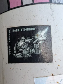 Street sticker A square, black-and-white sticker showing a futuristic armored soldier aiming and firing a rifle with a bright muzzle flash. Blocky text reading 'THE IRON WITHIN' borders the top and left sides.