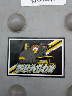 Street sticker Rectangular sticker featuring two masked football supporters, a beer mug, diagonal yellow and black stripes, and a yellow bus. The bottom displays 'BRASOV' in large, stylized grey letters.
