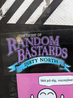 The sticker is predominantly black with a large, stylized purple font spelling out 'RANDOM BASTARDS'. Above this, in a smaller white font, is the text 'THE SECRET OF'. Below the main text, a light blue ribbon banner with a gradient effect contains the words 'DIRTY NORTH' in black, sans-serif font. The entire design has a subtle white outline, giving it a raised appearance.