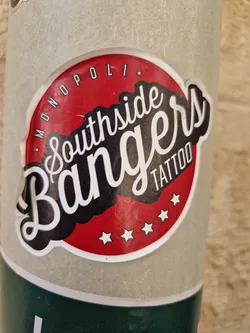 A round sticker with a red background and white stars. The text "Southside Bangers Tattoo" is written in a stylized font, with the words "Monopol." written in small letters around the top. 