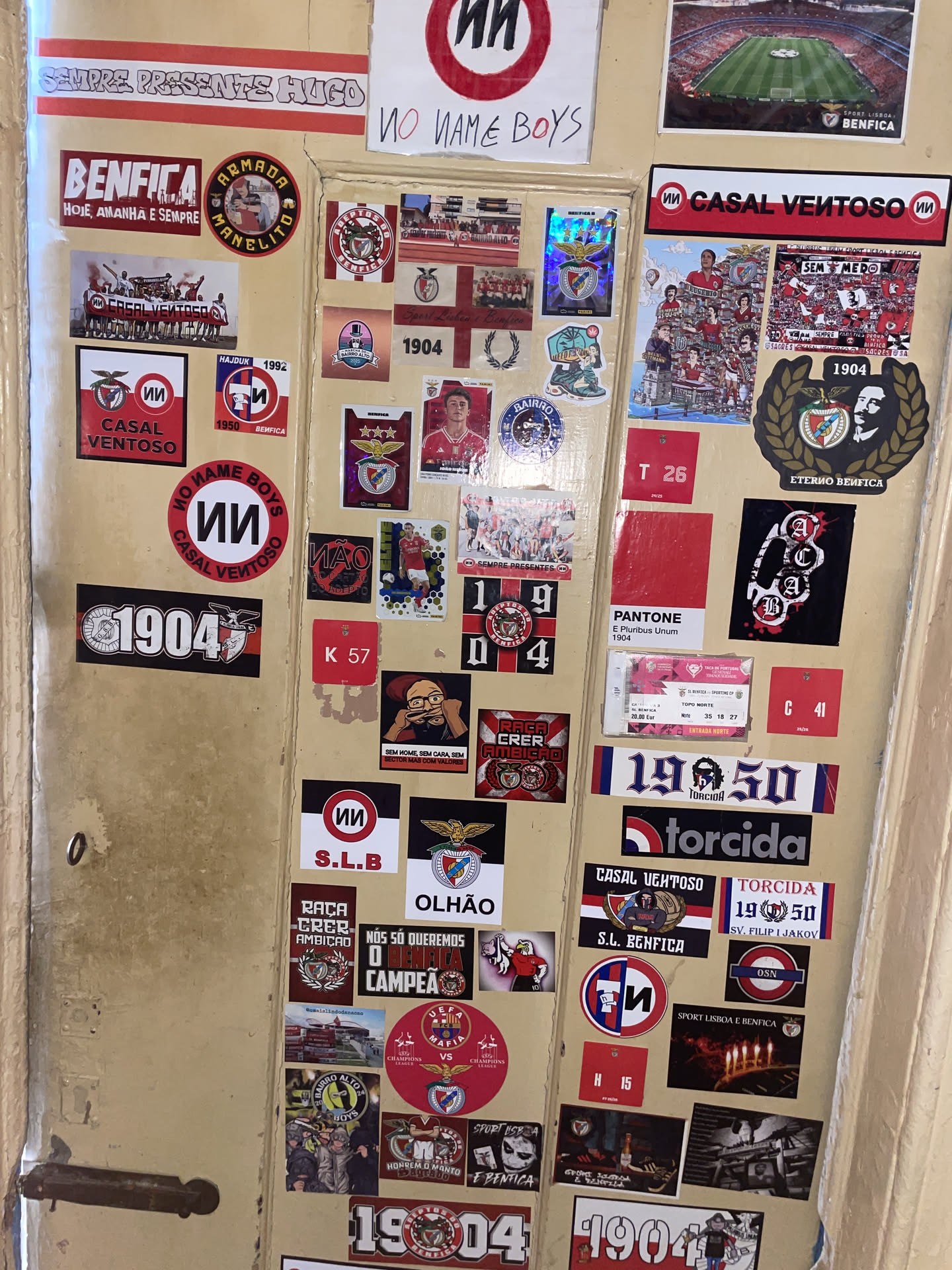 The sticker is circular, featuring a bold design with a red outer ring and a white inner circle. The top arc of the white circle displays the text 'NO NAME BOYS' in a strong, black, slightly stylized font. The bottom arc of the white circle reads 'CASAL VENTOSO' in a similar black font. Centered within the white circle is a distinctive stylized 'UU' symbol, also in black. The overall appearance is clean yet impactful, with the red, white, and black colors creating a striking contrast. The sticker shows minor signs of wear, consistent with a physical adhesive item.