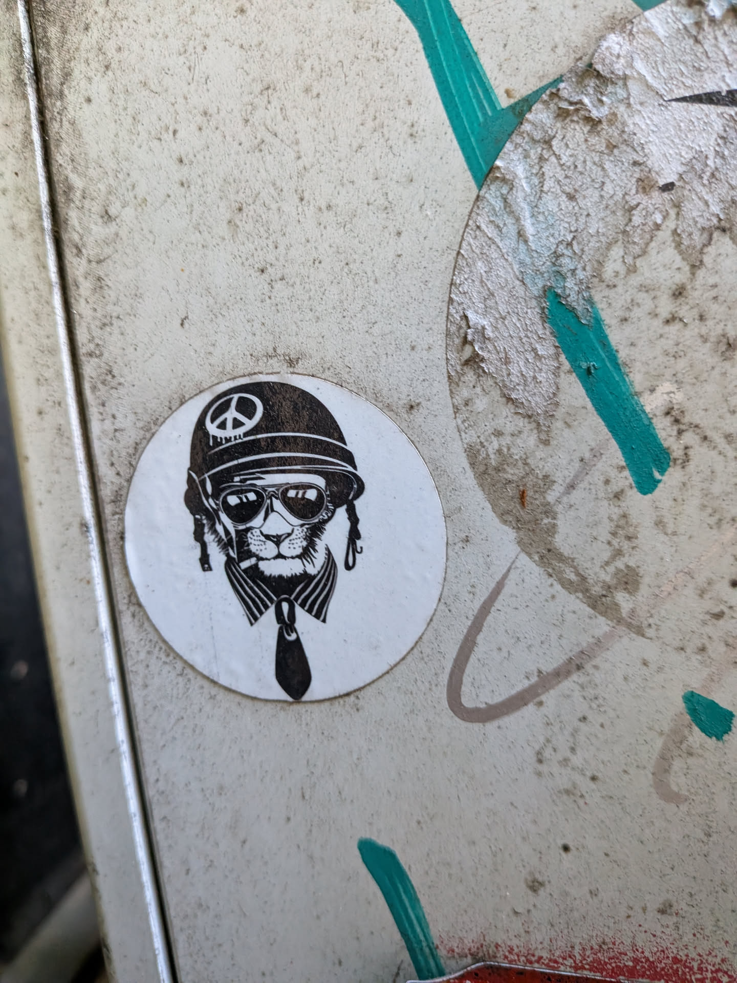 Circular white sticker with a black ink drawing of a cat wearing a peace-sign helmet, sunglasses, and a tie.