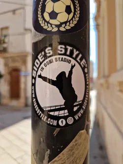 Street sticker A black and white sticker with a silhouette of a person celebrating a goal in a soccer stadium. The text around the circle says "Side's Style" and "In Ogni Stadio" (In Every Stadium).  There are Facebook and Instagram icons on the sticker.  Another sticker featuring a soccer ball is visible above it.