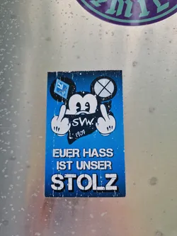 Street sticker A blue sticker featuring a Mickey Mouse parody giving the middle finger. The text says "Euer Hass Ist Unser Stolz", which translates to "Your hate is our pride". The sticker includes a logo that appears to be SWM 1907.