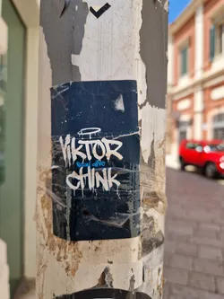 A dark-blue sticker with graffiti-style text reading "Viktor" over "Stay alive" over "Chink" is stuck to a weathered pillar. The sticker shows some signs of wear and tear.