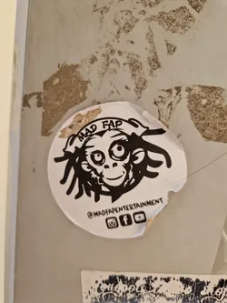 Street sticker A round sticker with a black and white illustration of a monkey with dreadlocks. The text "MAD FAP" is written above the monkey, and "@MADFAPENTERTAINMENT" is written below. Social media icons for Instagram, Facebook, and YouTube are also included.