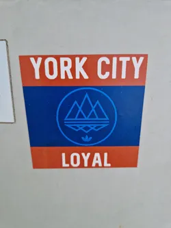 Street sticker A sticker featuring the text "YORK CITY" at the top, a logo with three stylized mountains and the Adidas logo in the center, and the text "LOYAL" at the bottom. The colors used are blue, orange and white.