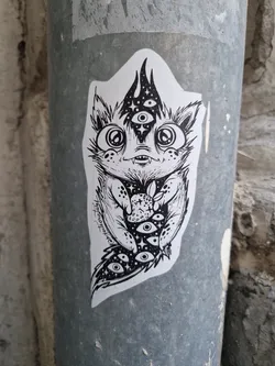 Street sticker Black and white illustration of a cute monster cat holding a strawberry. It has multiple eyes and mystical vibes. The artwork is on a sticker.