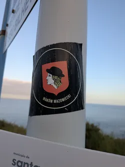A black square sticker featuring a circular emblem. Inside, a red shield depicts a blonde profile wearing a black hat. Below the shield, the text 'MAKÓW MAZOWIECKI' is printed in white.