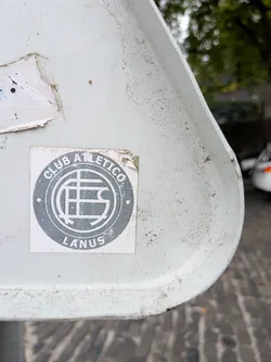 Street sticker A square sticker with a circular grey emblem. It features the text 'CLUB ATLETICO' and 'LANUS' wrapped around a central stylized monogram on a white background.