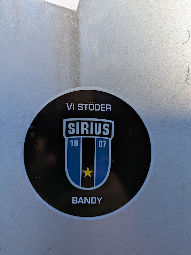 A round sticker featuring the logo of Sirius Bandy, a Swedish bandy team. The logo includes the text "VI STÖDER SIRIUS" and the year "1907". The design incorporates blue and black vertical stripes with a yellow star at the bottom. The word "BANDY" is printed below the logo.