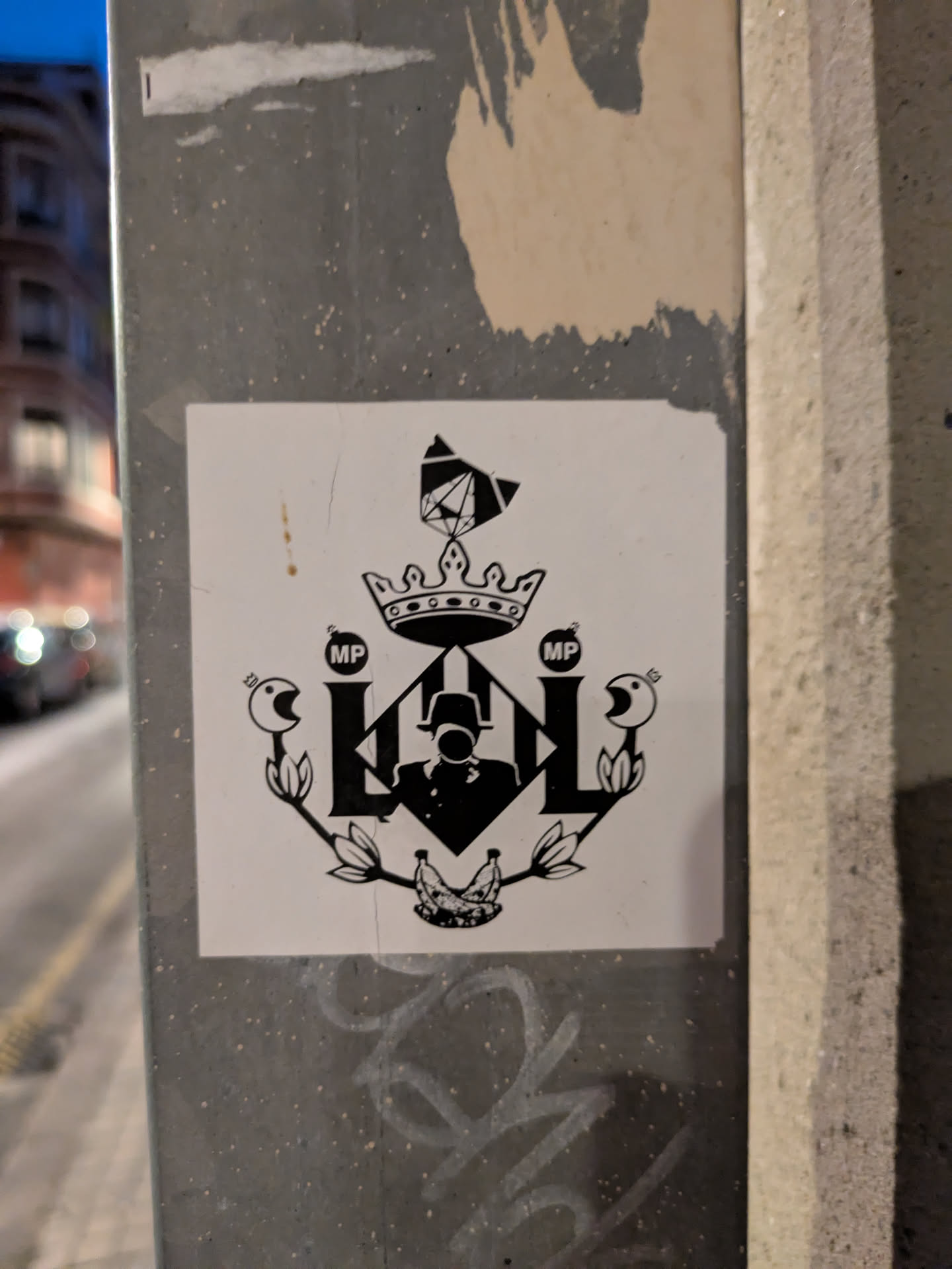 This sticker displays a black and white heraldic-style design. The letters "LOL" are prominent, flanked by stylized birds holding bombs marked "MP." A crown sits atop the "LOL," with an additional element above the crown. A silhouette of a figure in a hat is positioned within the center of the "LOL," and a pair of bananas are at the bottom. The overall design mimics a crest or coat of arms.
