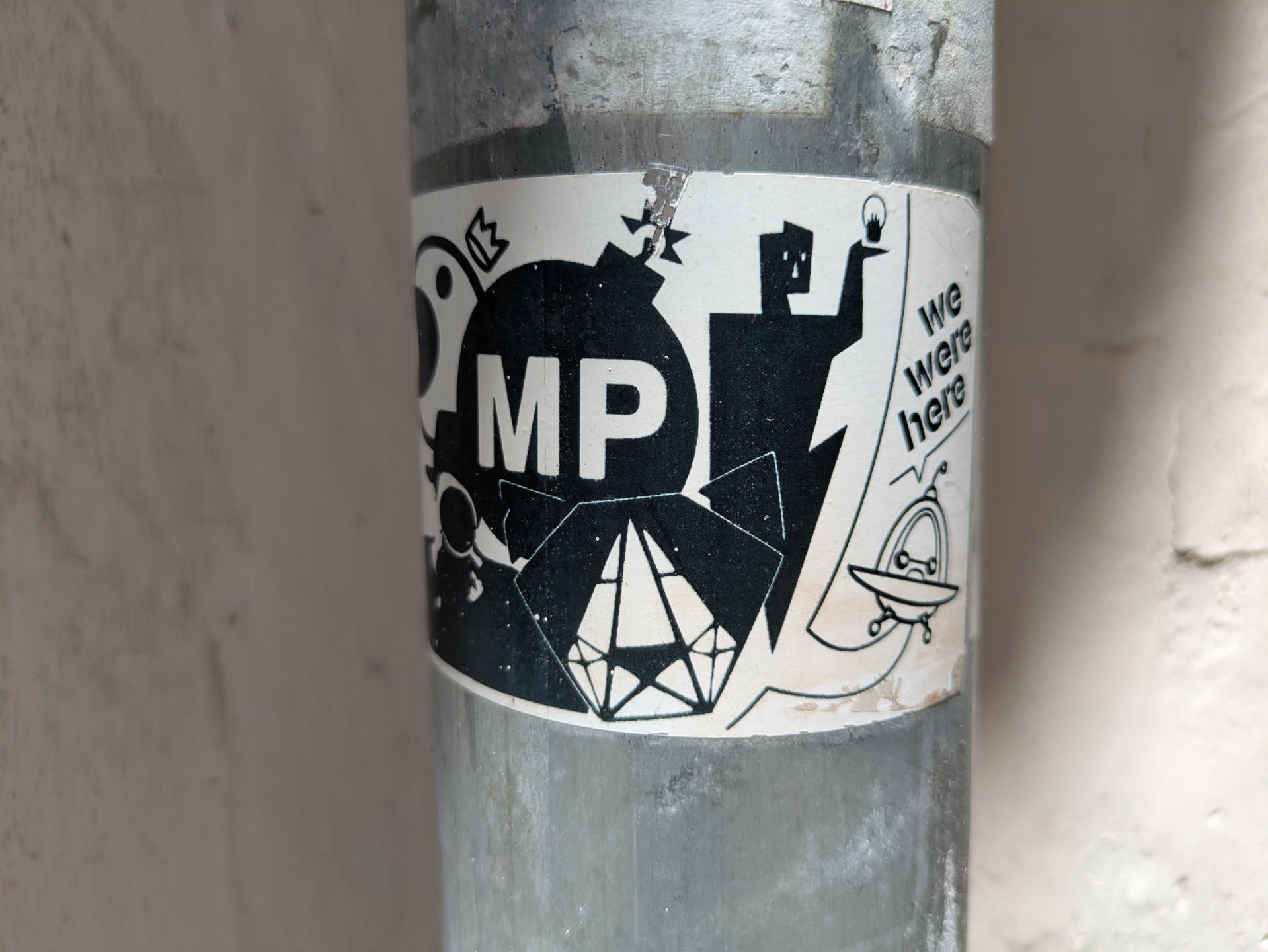 The sticker features a bomb with the letters 'MP' on it, a figure holding a lightbulb, a diamond shape, and a UFO. The text 'we were here' is also included.