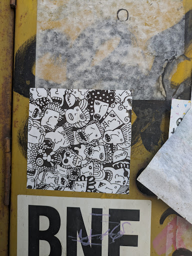 A black and white sticker features a densely packed illustration of faces with varying expressions and styles. The faces are drawn in a doodle-like manner with thick black lines, creating a playful and chaotic composition. The white background is completely filled with the illustration.