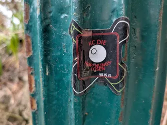 Street sticker An X-shaped black sticker featuring a red square border. Inside, a central white eyeball graphic is flanked by a green hand grenade icon and white tally marks. The red text reads 'KC DIE HOFFNUNGSLOSEN'.