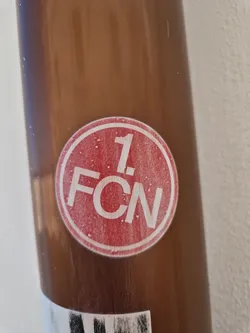 Street sticker A red and white circular sticker with the text "1. FCN" inside.  The sticker is attached to a brown surface. The number 1 is prominently featured above the letters.