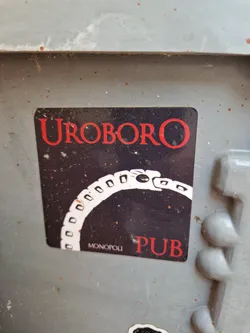 Street sticker A sticker featuring the word "UROBORO" in red lettering above an image of a snake eating its tail, with "MONOPOLI PUB" written at the bottom. The background is dark with a starry appearance.