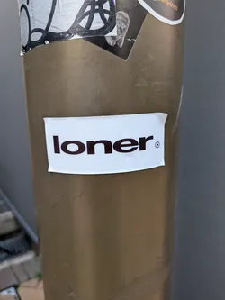 Street sticker A simple white rectangular sticker displaying the word 'loner' in bold black lowercase letters, followed by a small circular play icon.