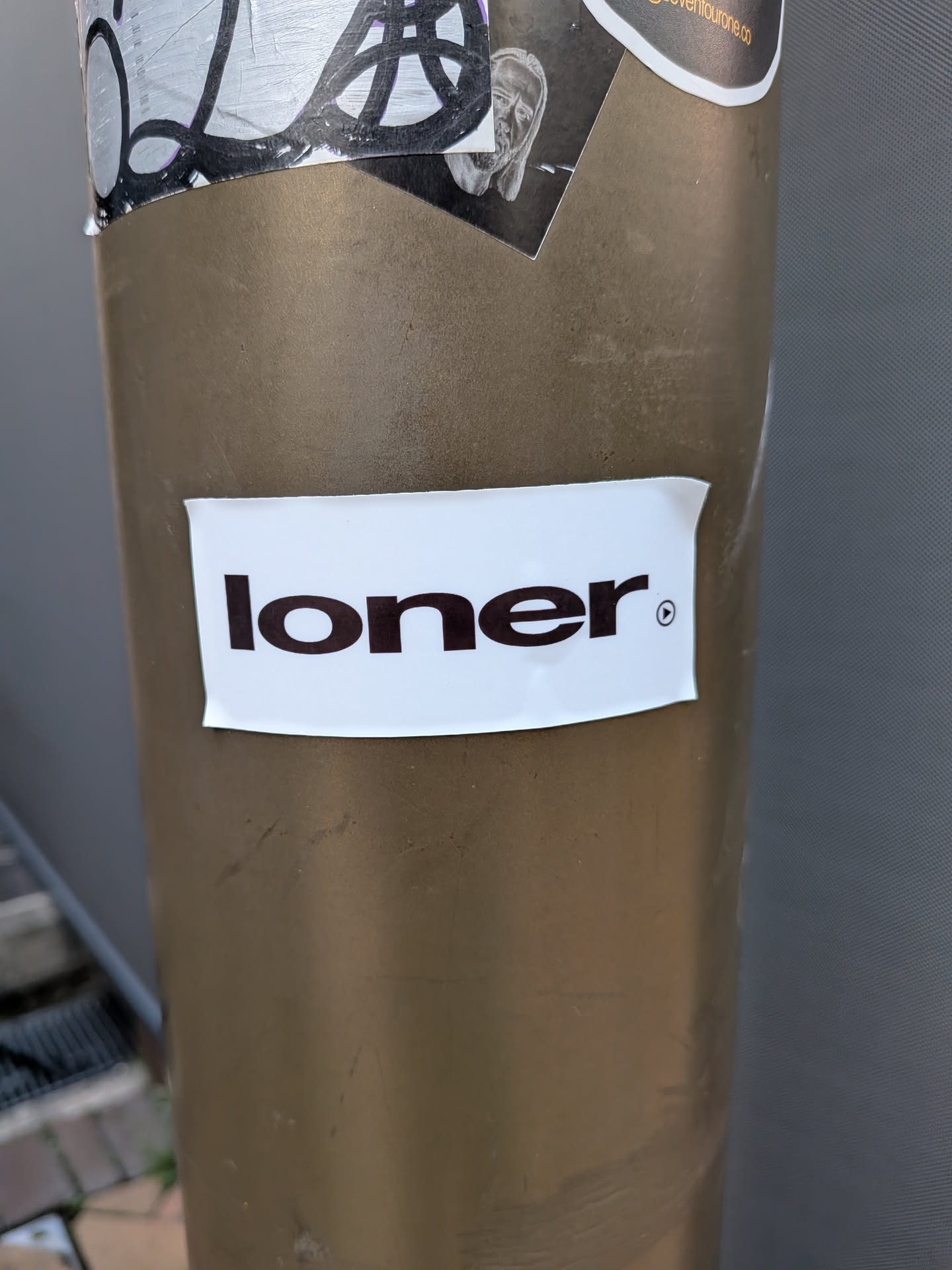 A simple white rectangular sticker displaying the word 'loner' in bold black lowercase letters, followed by a small circular play icon.
