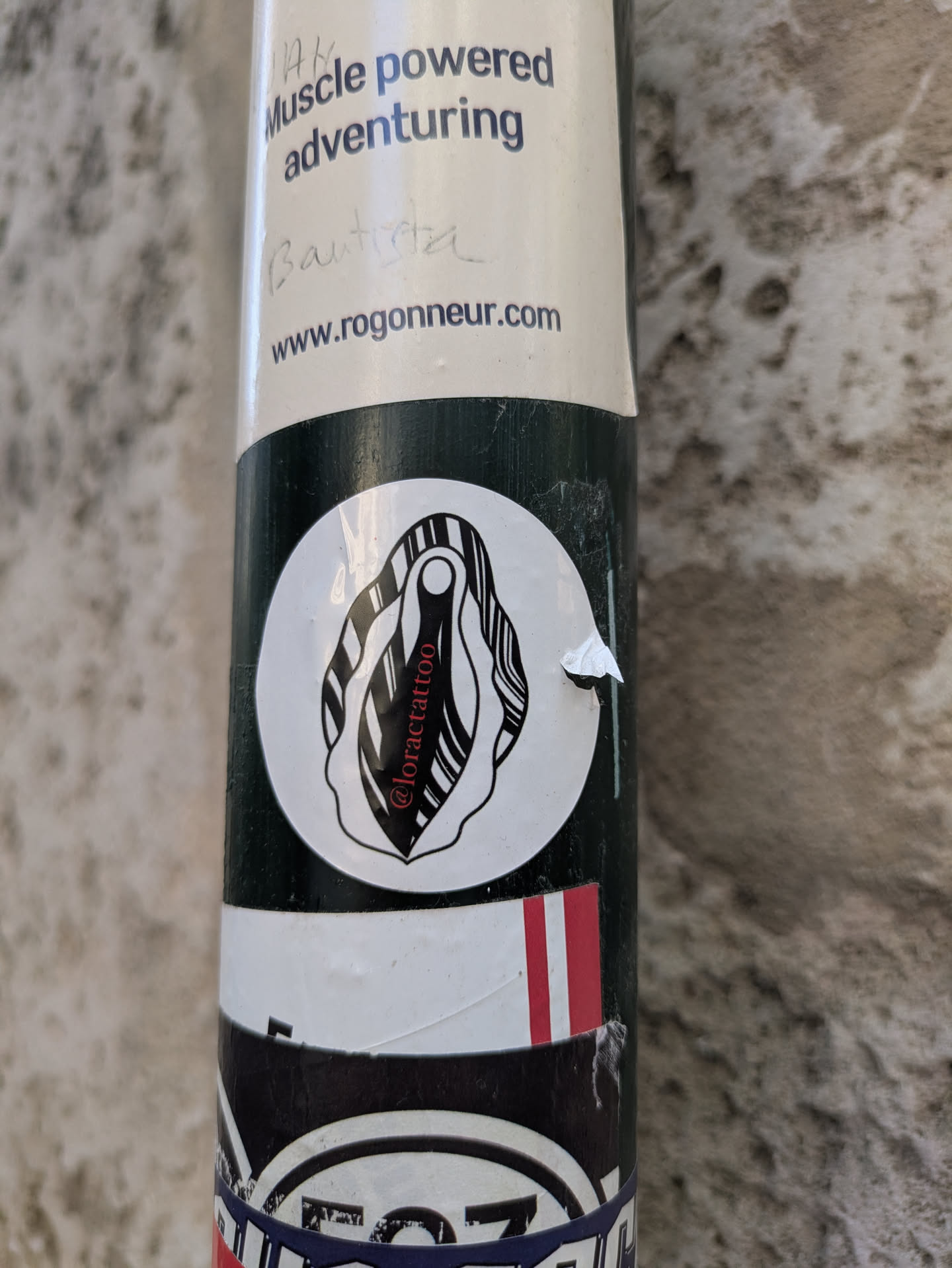 The sticker is circular with a white background. The design features a stylized vulva outlined in black with alternating black and white stripes filling the interior. The Instagram handle "@loractattoo" is written in red script on the right side of the vulva design.