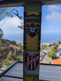 Street sticker A vertical rectangular sticker with a yellow and dark blue color scheme. It features a central crest with a bridge, waves, a soccer ball, and a laurel wreath. Text at the top reads 'ABOBRIGA F.C.' and cursive text at the bottom reads 'Catro elementos unha conquista'.