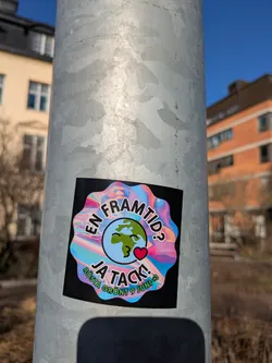 Street sticker A square sticker with rounded corners on a metal pole. The main design features a colorful, marbled background framing a globe with a smiley face and a heart. The text reads "En Framtid? Ja Tack!" and "Rösta Grönt 9 Juni" suggesting a call to vote green. It is an environmental advocacy.