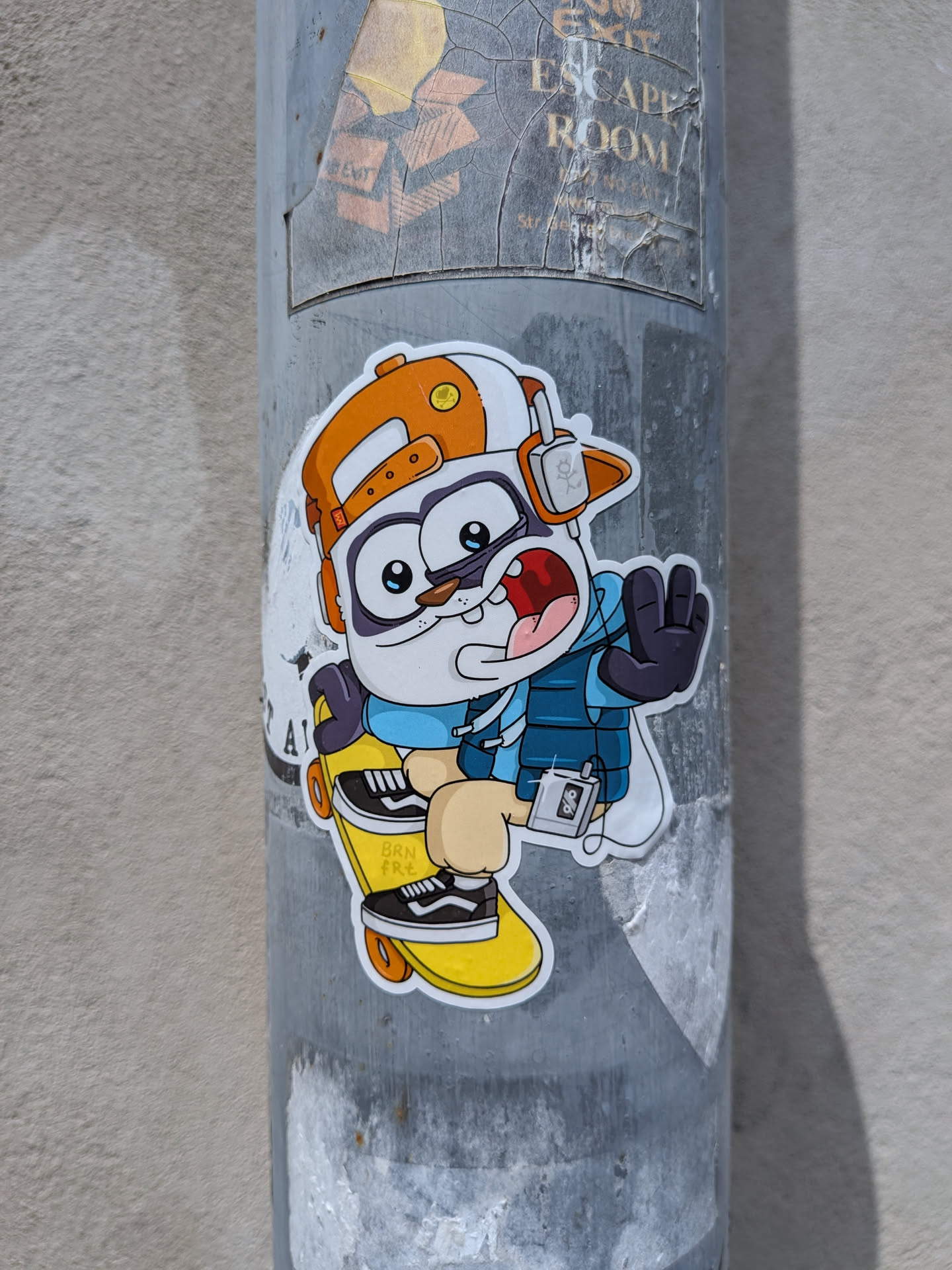Die-cut sticker of a cartoon animal character wearing an orange cap, blue vest, and headphones while riding a yellow skateboard.