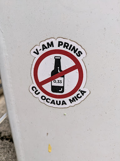 This is a sticker that features a bottle, with the size 0.33 on it, inside a red circle with a line through it, indicating "no alcohol". Above and below the circle is the text "V-AM PRINS CU OCAUA MICA."