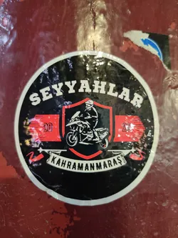 Street sticker A round black sticker with a white border. It features a central red shield containing a motorcyclist illustration, flanked by red banners with the number '20'. The top text reads 'SEYYAHLAR' and the bottom banner reads 'KAHRAMANMARAŞ'.