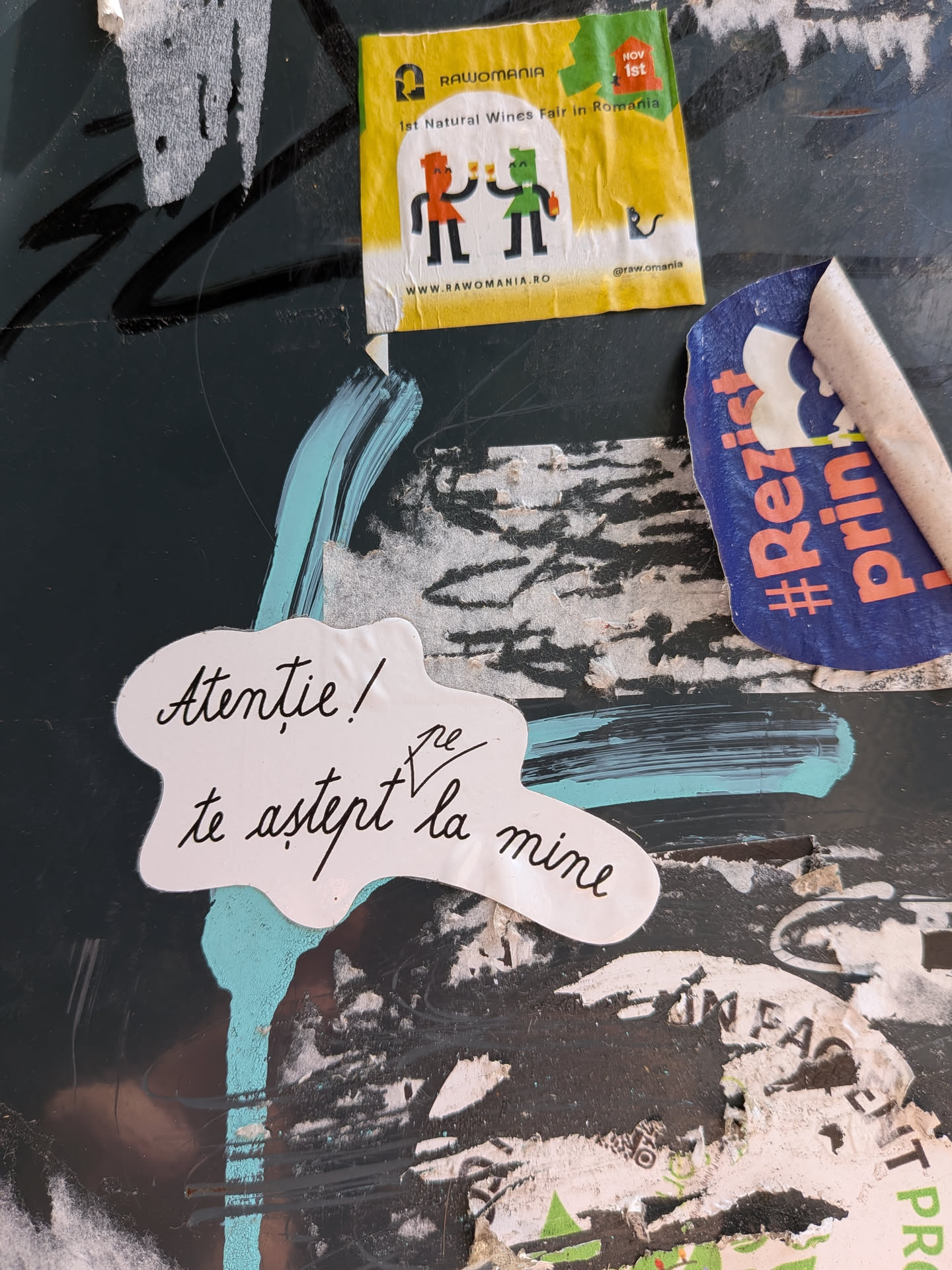 A die-cut, cloud-shaped white sticker featuring black cursive handwriting in Romanian. It is pasted on a dark, textured wall over blue paint streaks.