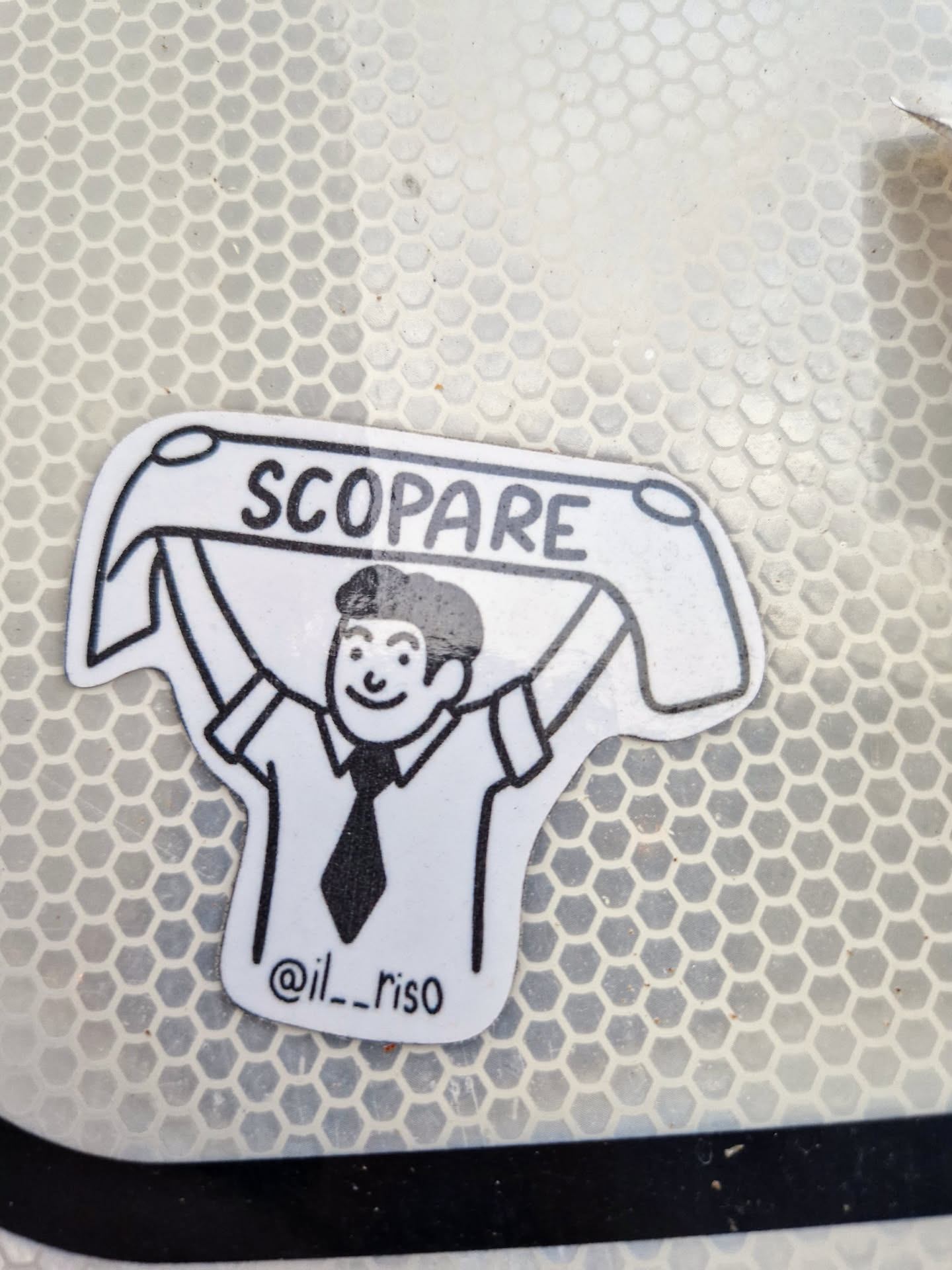 A black and white illustration style sticker features a man holding a banner that says "SCOPARE" in all caps. Below the figure, it reads "@il__riso".