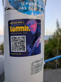A rectangular dark blue sticker featuring a guitarist in pink and blue lighting, yellow promotional text, a QR code, and the website tommin.de.