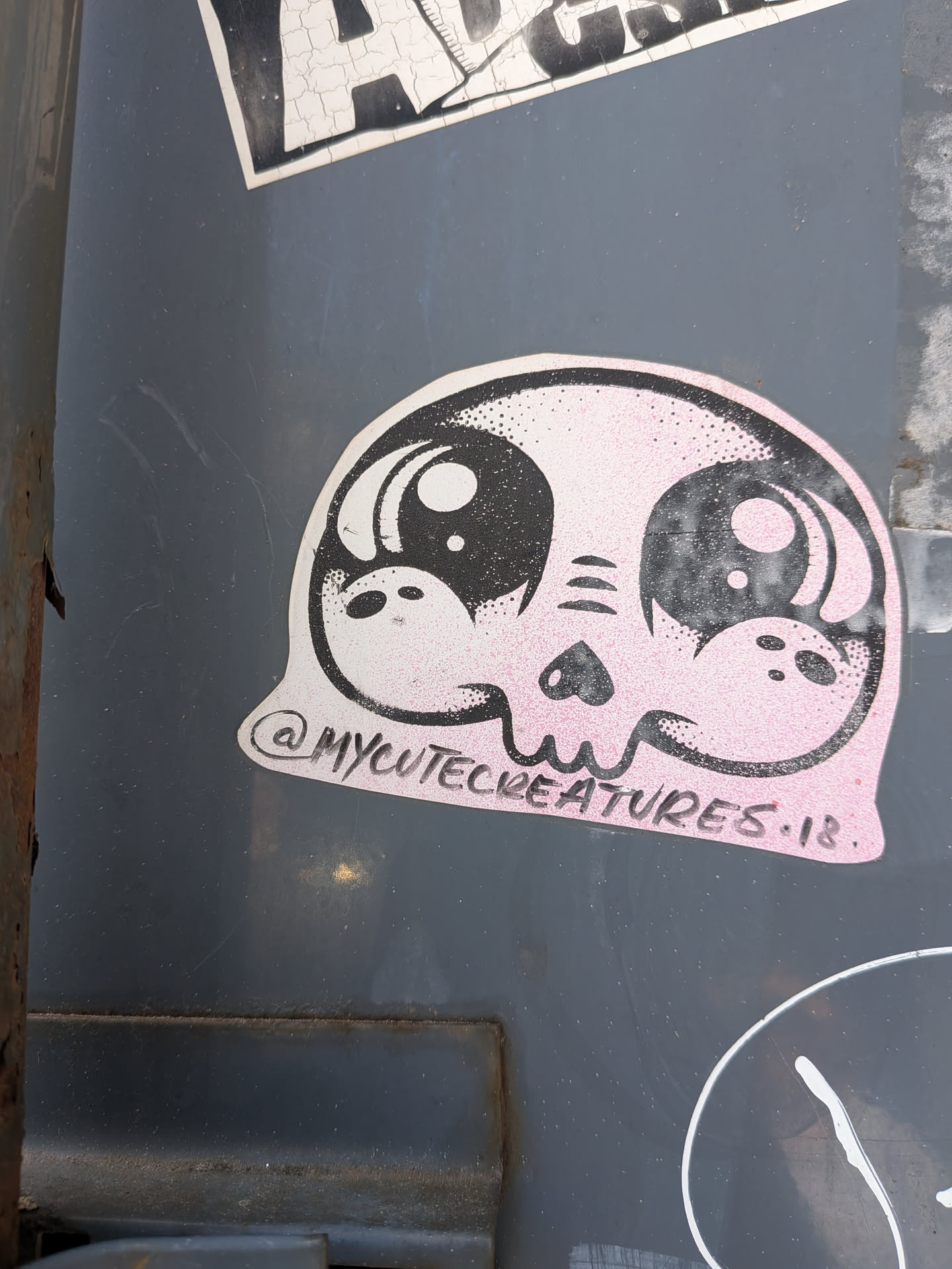 A die-cut sticker of a stylized pink skull with oversized, glossy anime-style eyes. Features stippled black shading and the handle '@MYCUTECREATURES.18.' printed along the bottom curve.